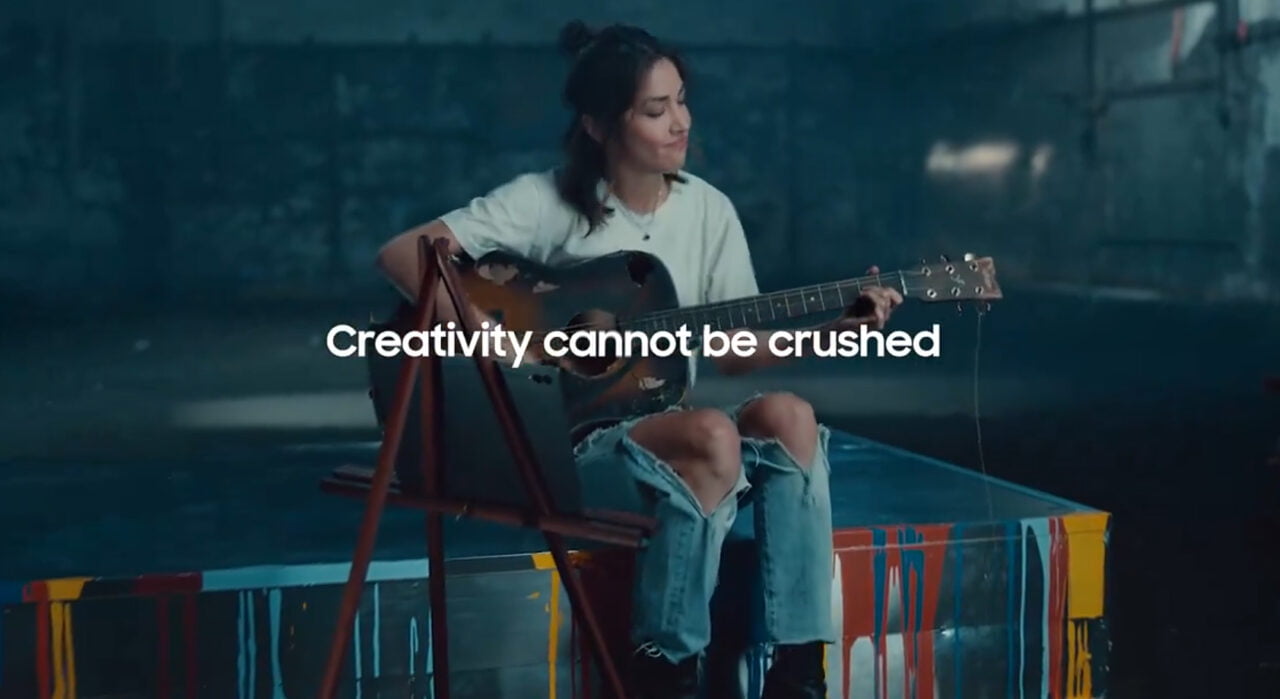 Zrzut ekranu z reklamy Samsunga. Kobieta grająca na gitarze z tekstem "Creativity cannot be crushed" na ekranie.