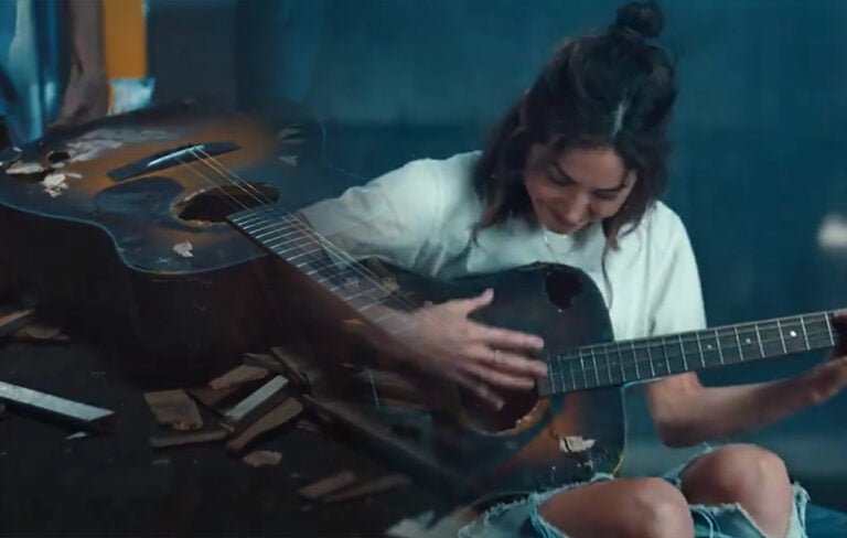 Kobieta grająca na mocno zniszczonej gitarze akustycznej.