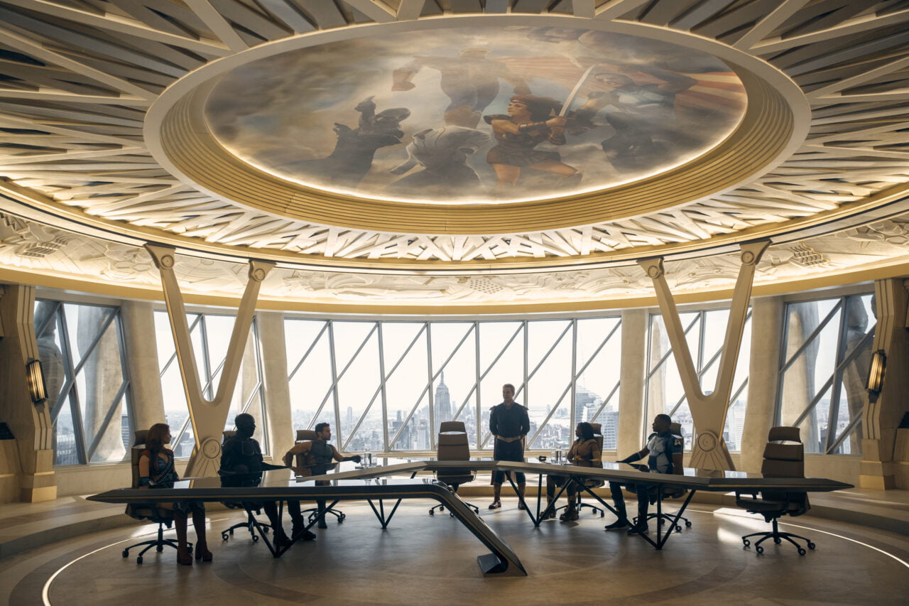kadr z serialu The Boys 4 od Amazon Prime Video. Nowoczesna sala konferencyjna z dużym okrągłym sufitem z malowidłem i panoramicznymi oknami, przez które widać miasto. Szereg osób siedzi przy zakrzywionym stole, jedna z nich stoi.
