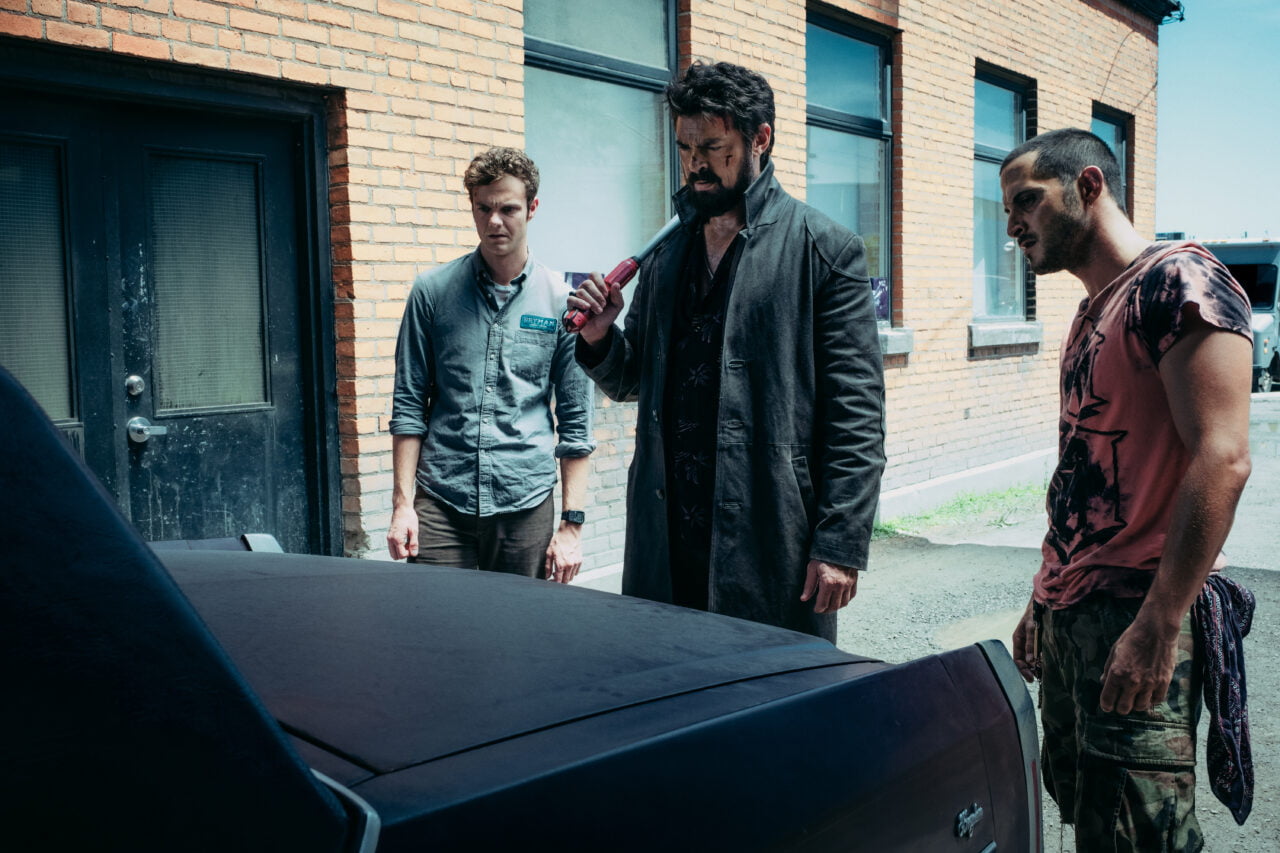 Kadr z The Boys od Amazon Prime Video. Trzech mężczyzn stoi obok samochodu na tle ceglanego budynku.