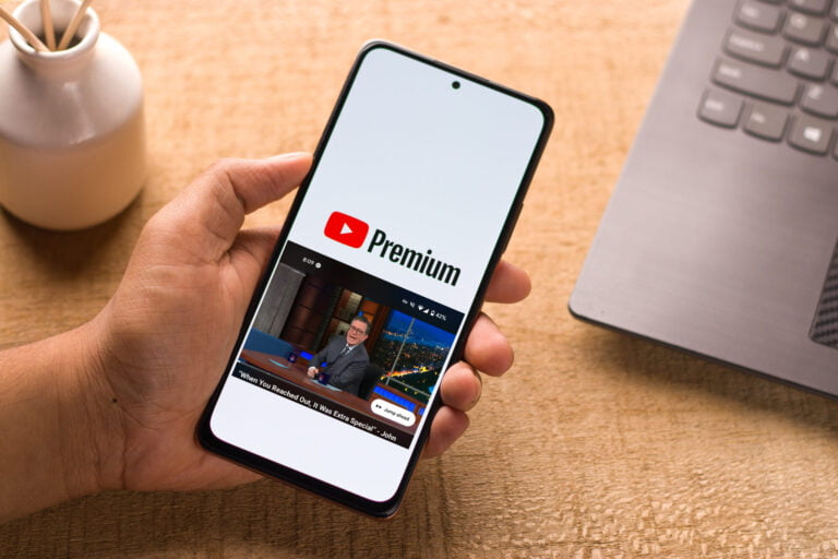 Dłoń trzymająca smartfon z otwartą aplikacją YouTube Premium, wyświetlającą wideo z mężczyzną siedzącym przy biurku.