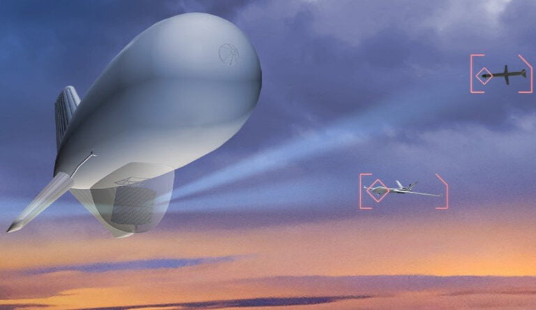 Aerostat przemieszczający się na tle zachodzącego słońca z dwoma mniejszymi samolotami wskazywanymi przez celowniki na prawo od balonu.