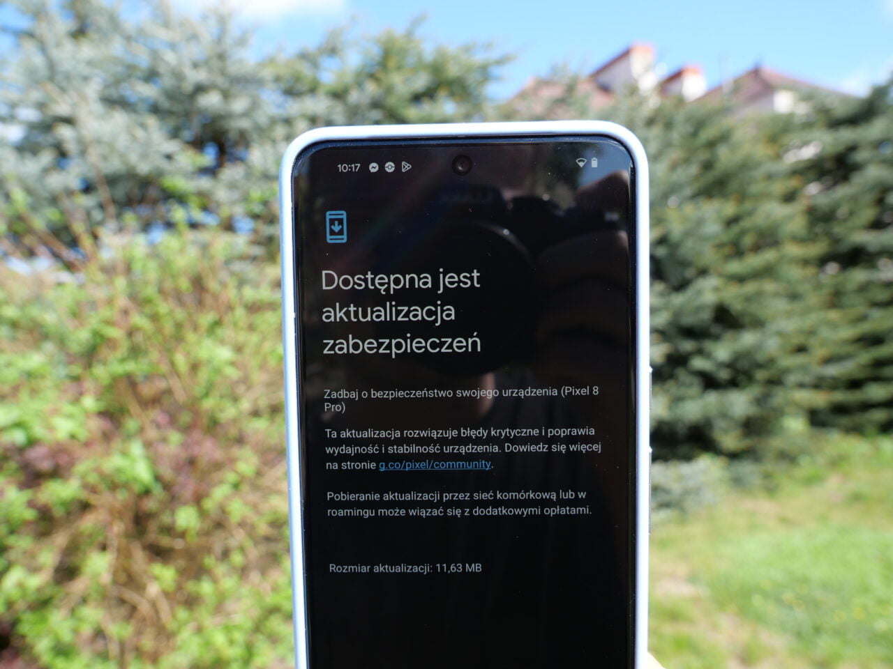 Smartfon wyświetlający komunikat o dostępnej aktualizacji zabezpieczeń, trzymany na tle rozmytego ogrodu.