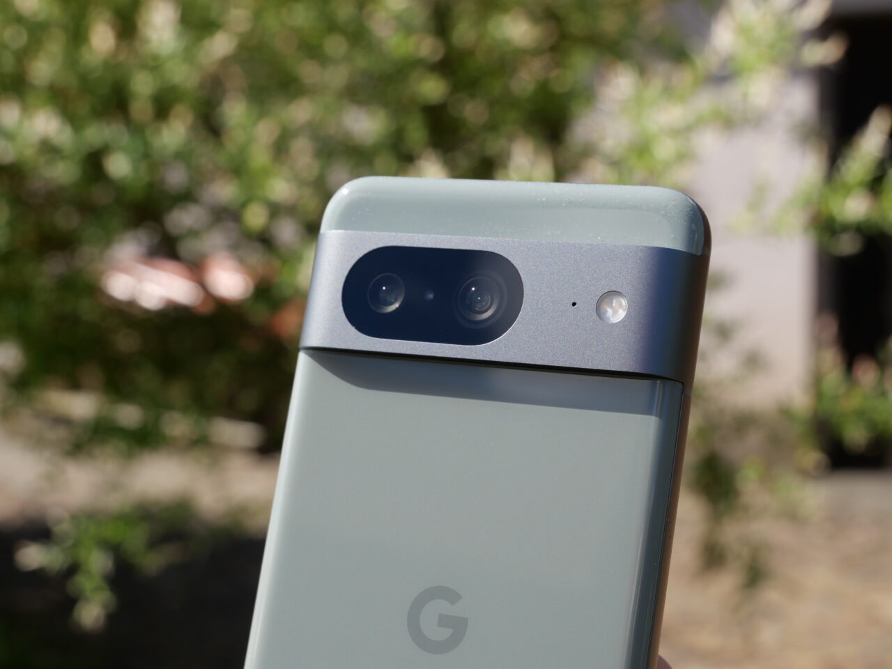Smartfon Google z podwójnym aparatem i logo na tylnej obudowie, trzymany na tle roślinności.