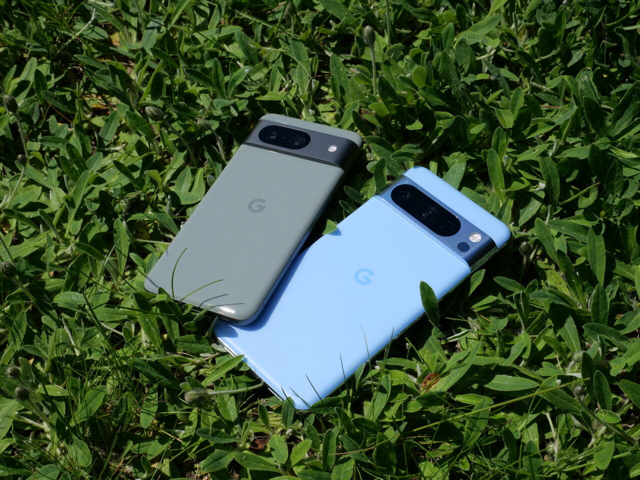 Dwa smartfony Google, jeden szary i jeden niebieski, na zielonej trawie.