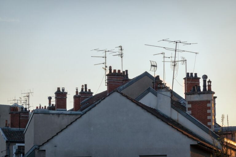 Dachy domów z kominami i antenami telewizyjnymi na tle wieczornego nieba.