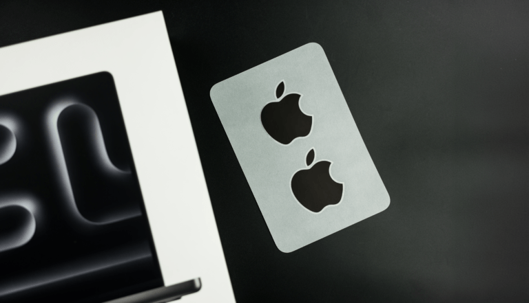 Naklejki z logo Apple obok kartonu po laptopie na ciemny blacie.