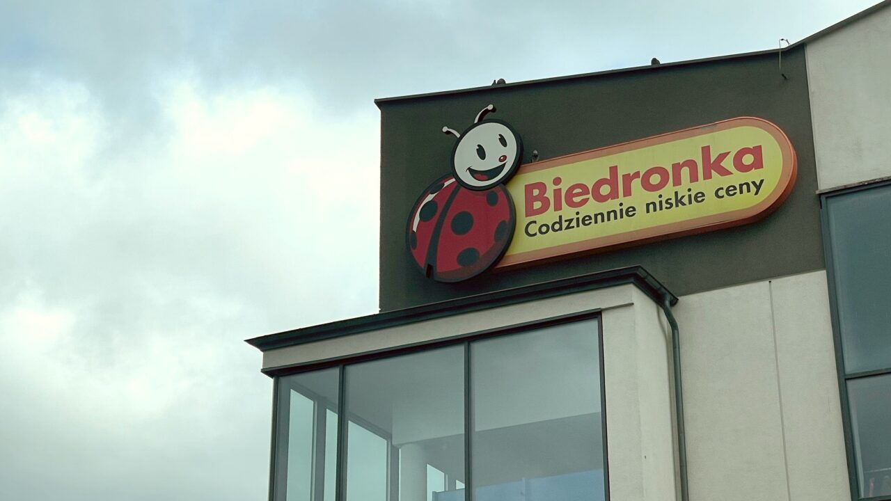 Znak sklepu Biedronka z logo w postaci uśmiechniętej biedronki, umieszczony na budynku, pod zachmurzonym niebem.
