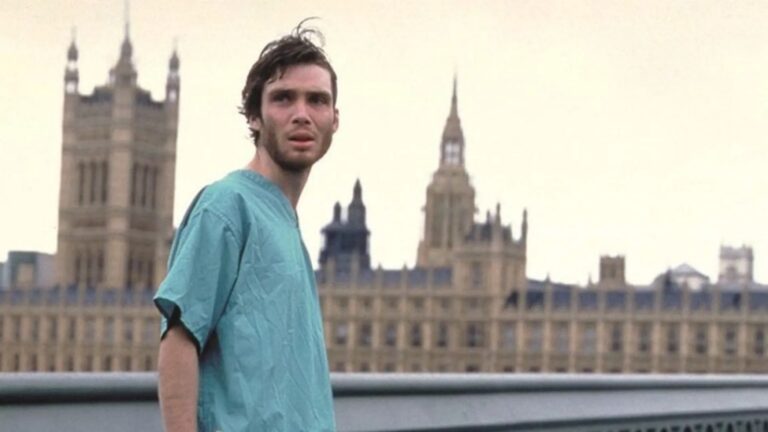 Mężczyzna w szpitalnej koszuli stoi przed budynkiem Parlamentu w Londynie.