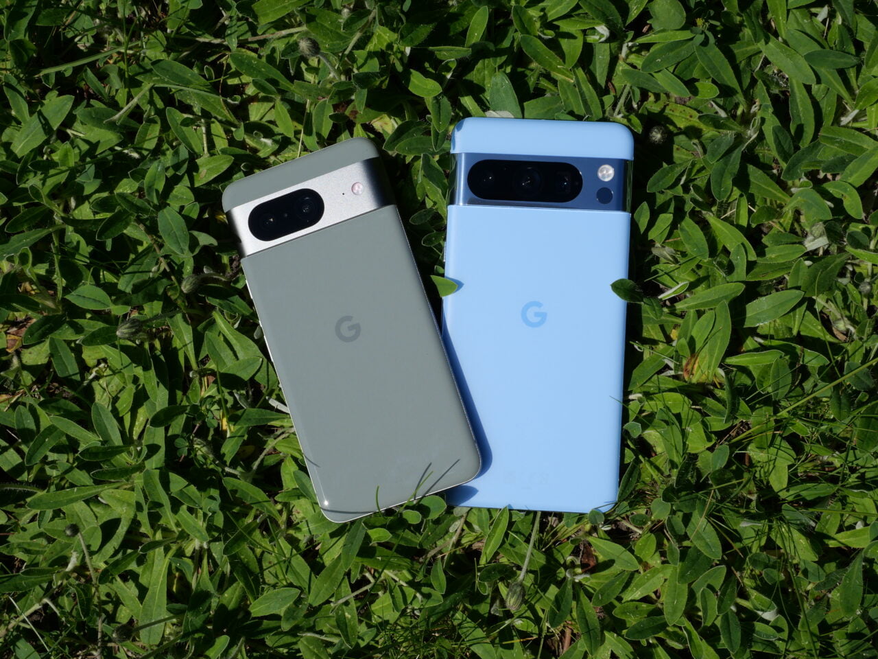 Dwa smartfony Google, jeden szary a drugi niebieski, leżące na zielonej trawie.