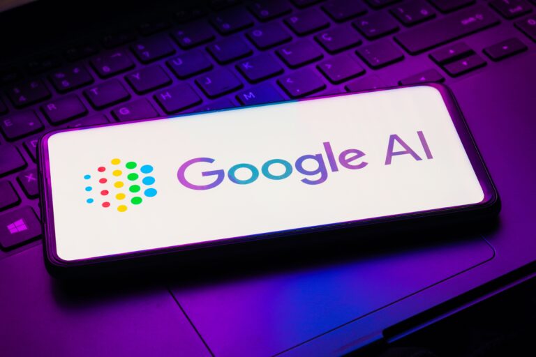 Telefon komórkowy z logo Google AI na ekranie, leżący na klawiaturze laptopa.
