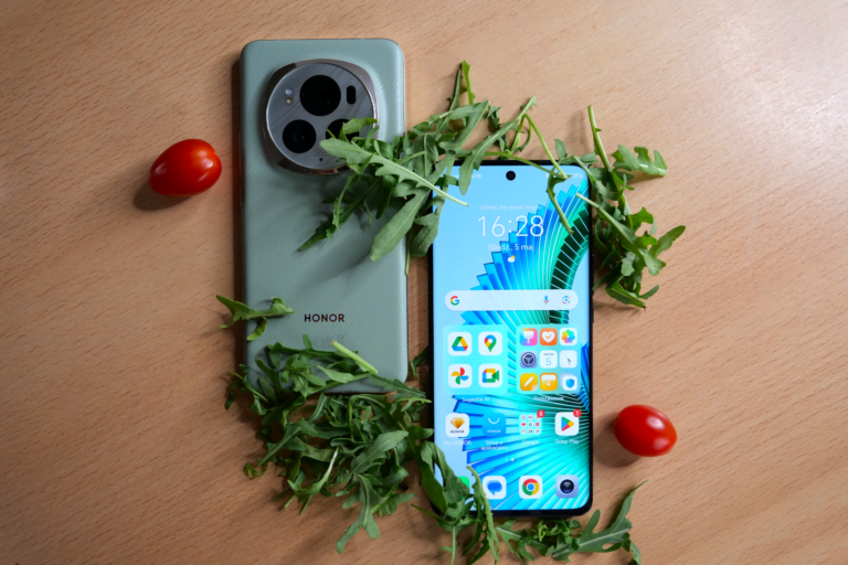 Dwa smartfony leżą na brązowy blacie w otoczeniu rukoli i pomidorków koktajlowych.