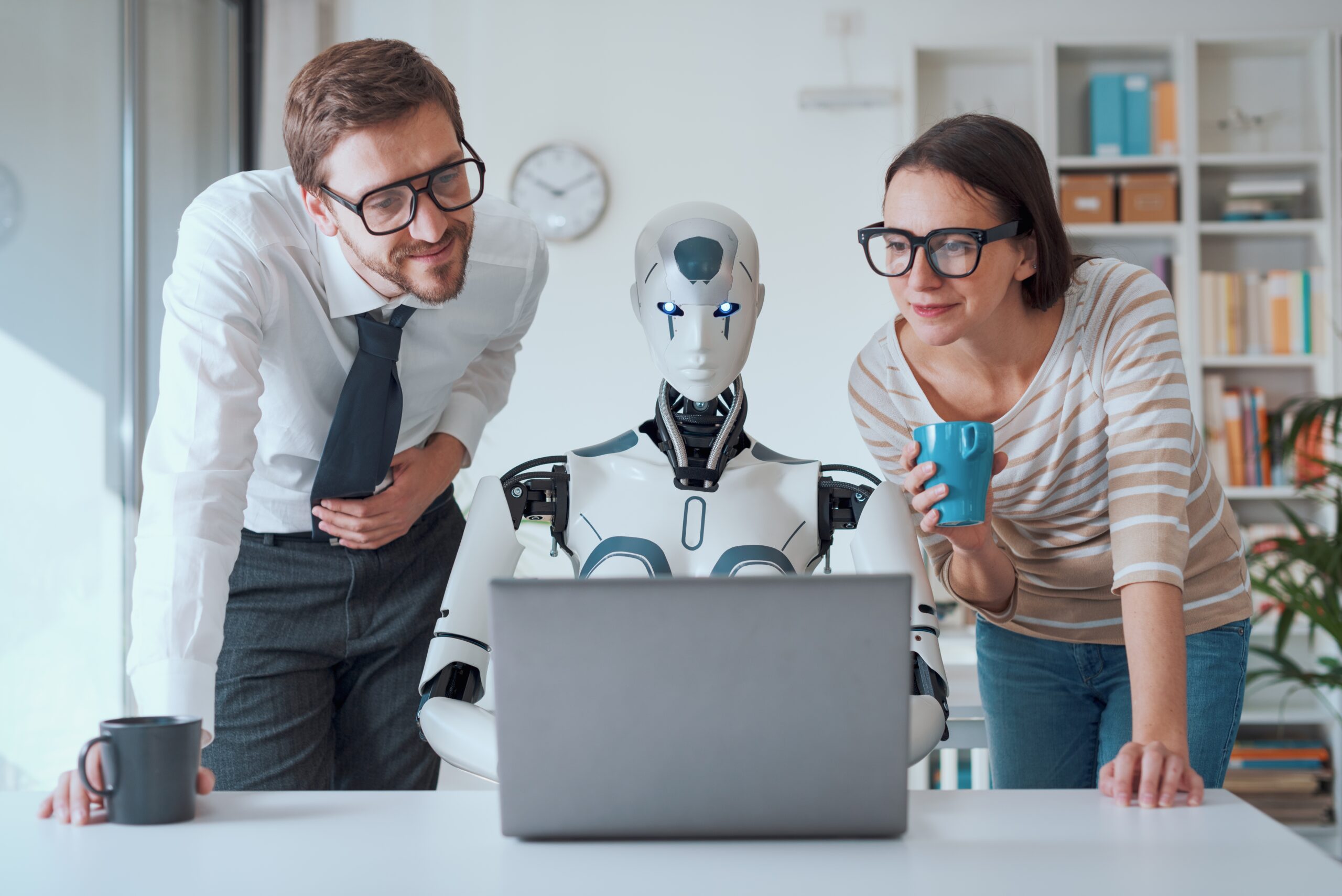 Dwoje ludzi i robot patrzą na laptopa w biurze.