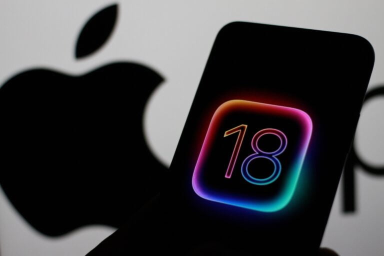 Telefon komórkowy z wyświetloną cyfrą 18 w tęczowych kolorach na tle rozmazanego logo Apple.