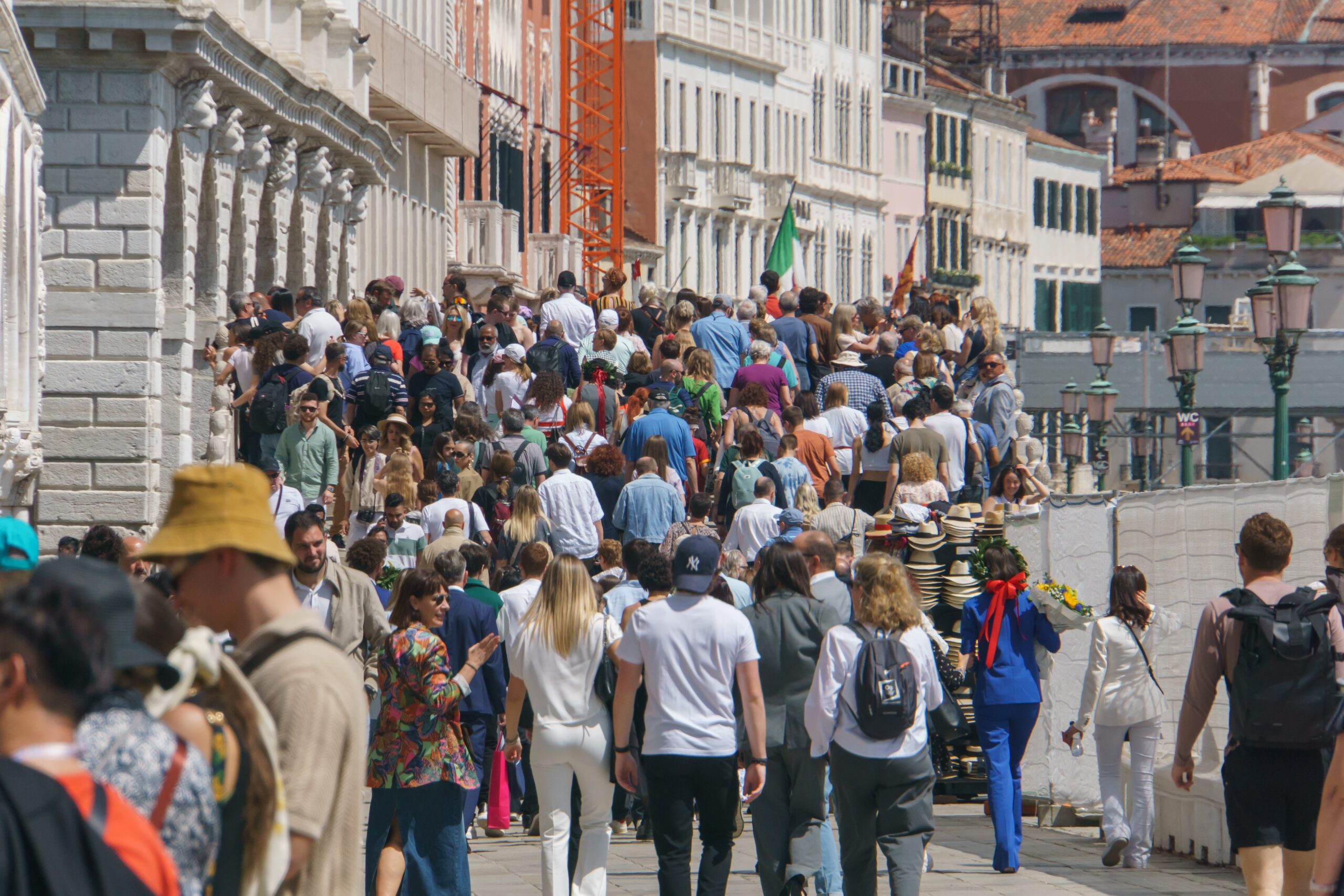 Duży tłum ludzi spacerujący wzdłuż wąskiej, zabytkowej uliczki w mieście. Ilu jest ludzi na świecie