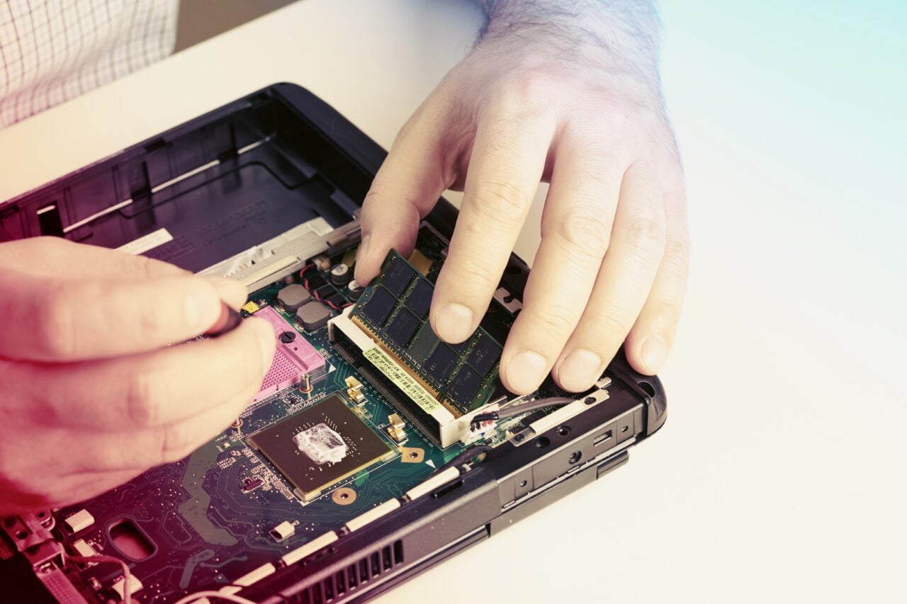 Ręce osoby instalującej pamięć RAM w otwartym laptopie.