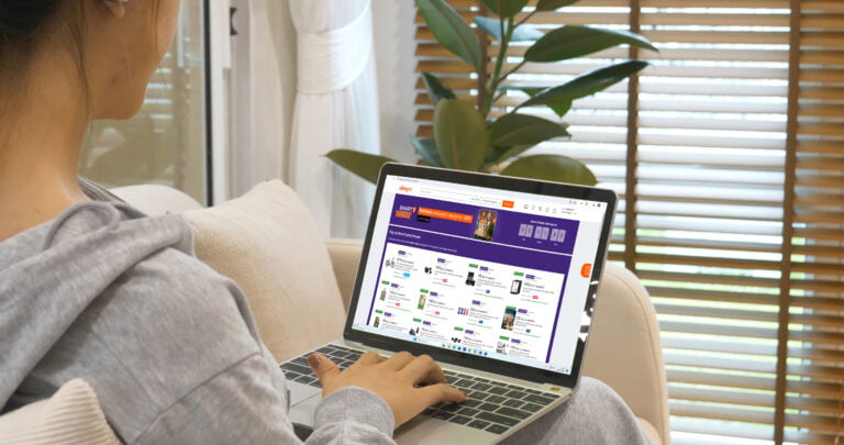 Kobieta przeglądająca stronę internetową Allegro na laptopie w jasnym, nowoczesnym wnętrzu mieszkania.