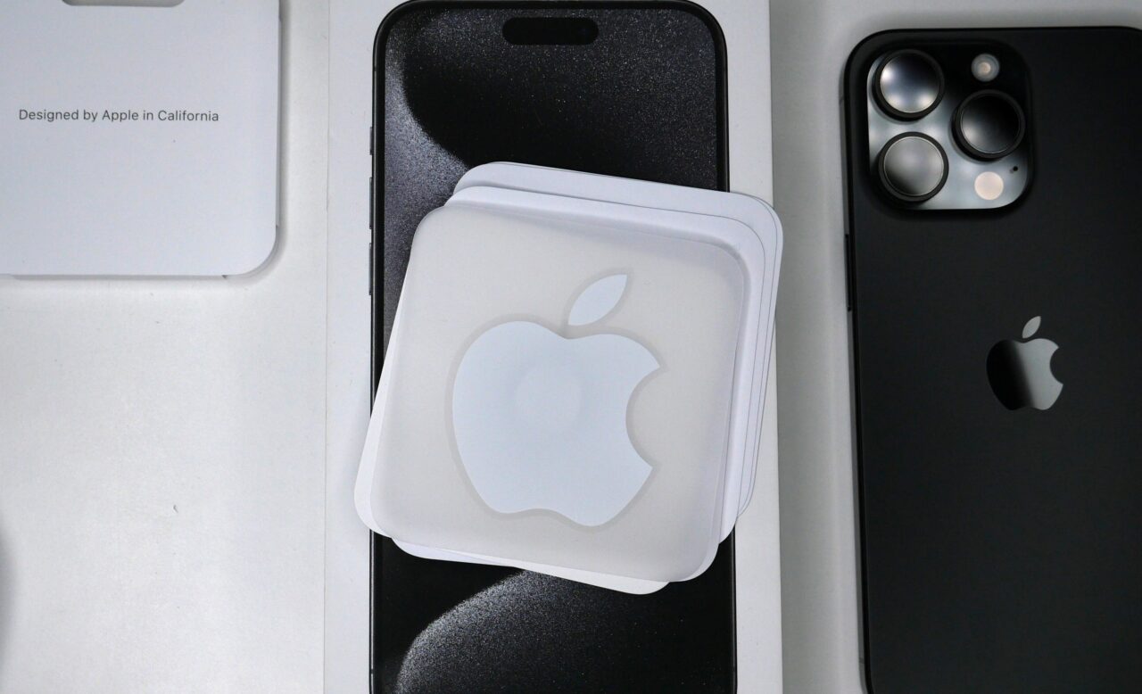 Zestaw produktów Apple, w tym iPhone z potrójnym aparatem, nakładki z logo Apple oraz opakowania z napisem "Designed by Apple in California".