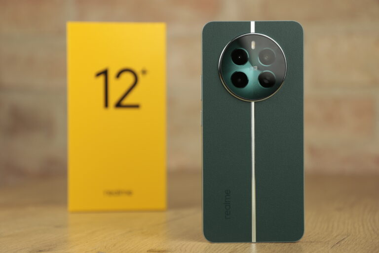 Zielony smartfon, recenzowane realme 12+ 5G z potrójnym aparatem i paskiem na tle drewnianej powierzchni oraz żółte opakowanie z napisem 12.
