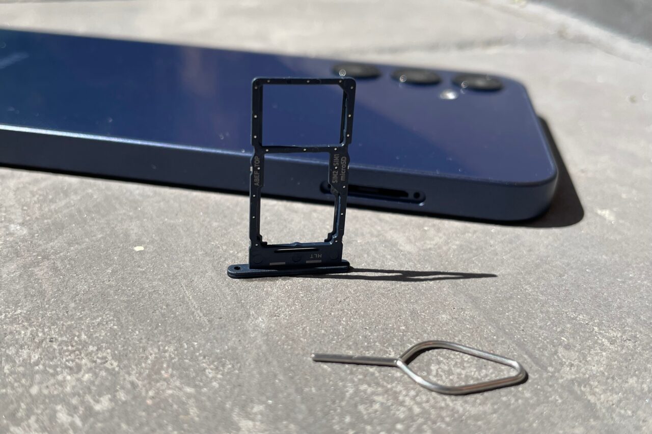 Zdjęcie ramki SIM, klucza do tacki SIM i niebieskiego smartfona leżącego na szarym betonie.