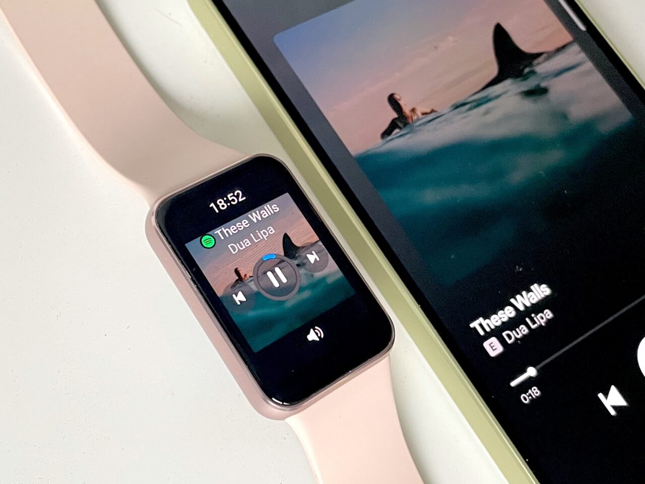 Smartwatch z różowym paskiem i smartfon odtwarzający piosenkę "These Walls" Dua Lipy na Spotify.
