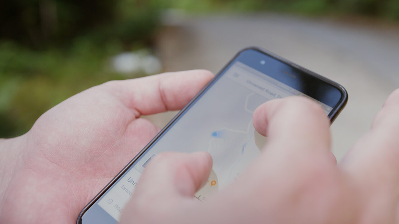 Dłonie trzymające smartfon wyświetlający mapę z oznaczoną lokalizacją na ekranie.