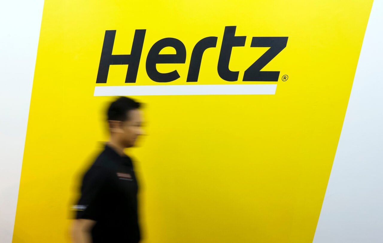 Mężczyzna przechodzący obok żółtego logotypu Hertz.