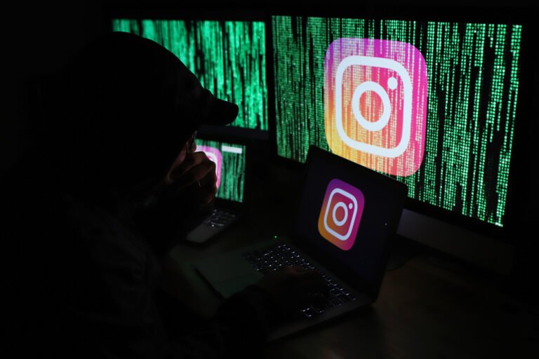 Osoba w kapturze pracuje na laptopach z wyświetlaczami przedstawiającymi logo Instagrama i zielone kody.