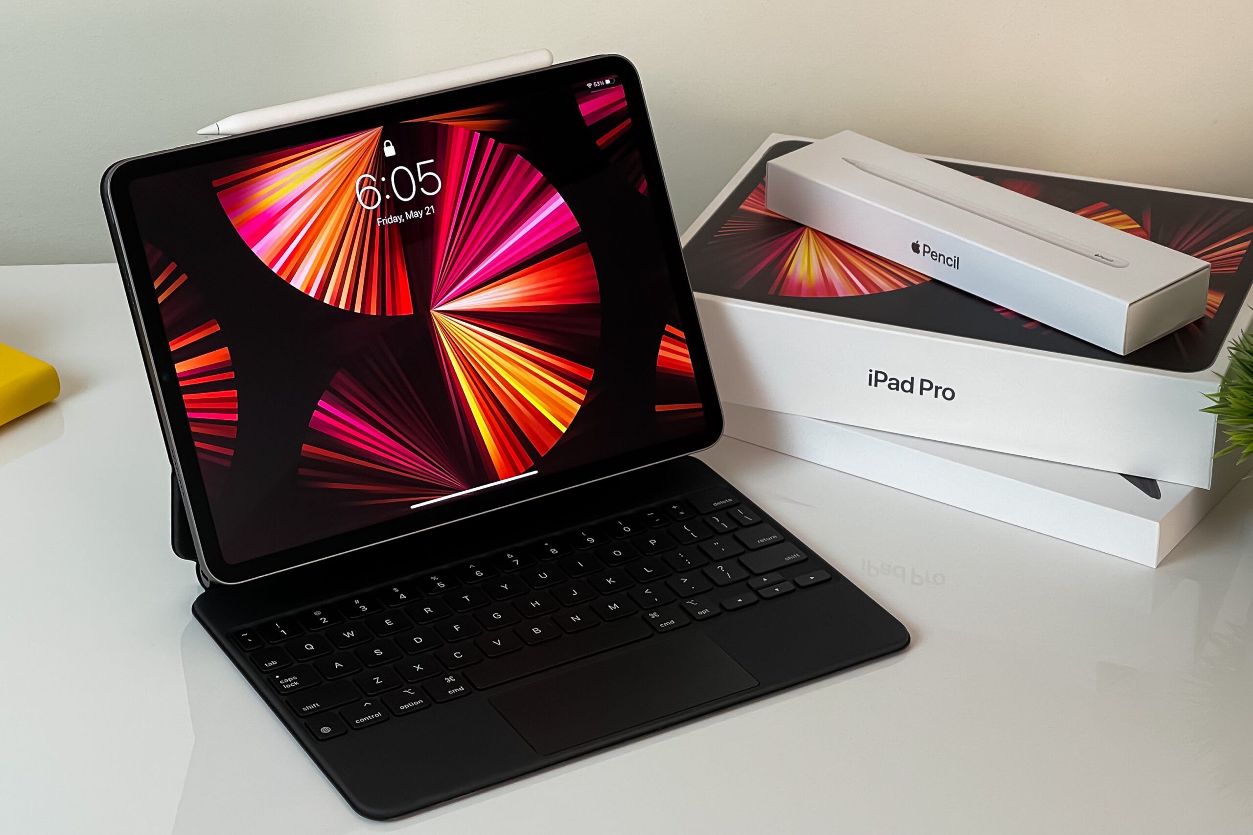 iPad Pro z klawiaturą na białym stole obok opakowań z iPencil i kartonem produktu.