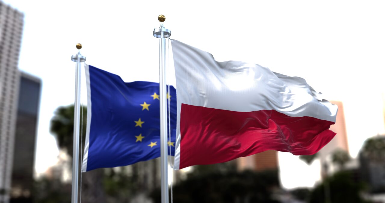 Europejski portfel cyfrowy coraz bliżej. Ministerstwo podało kluczową datę dla Polski Flagi Unii Europejskiej i Polski powiewające na tle miejskich drapaczy chmur.