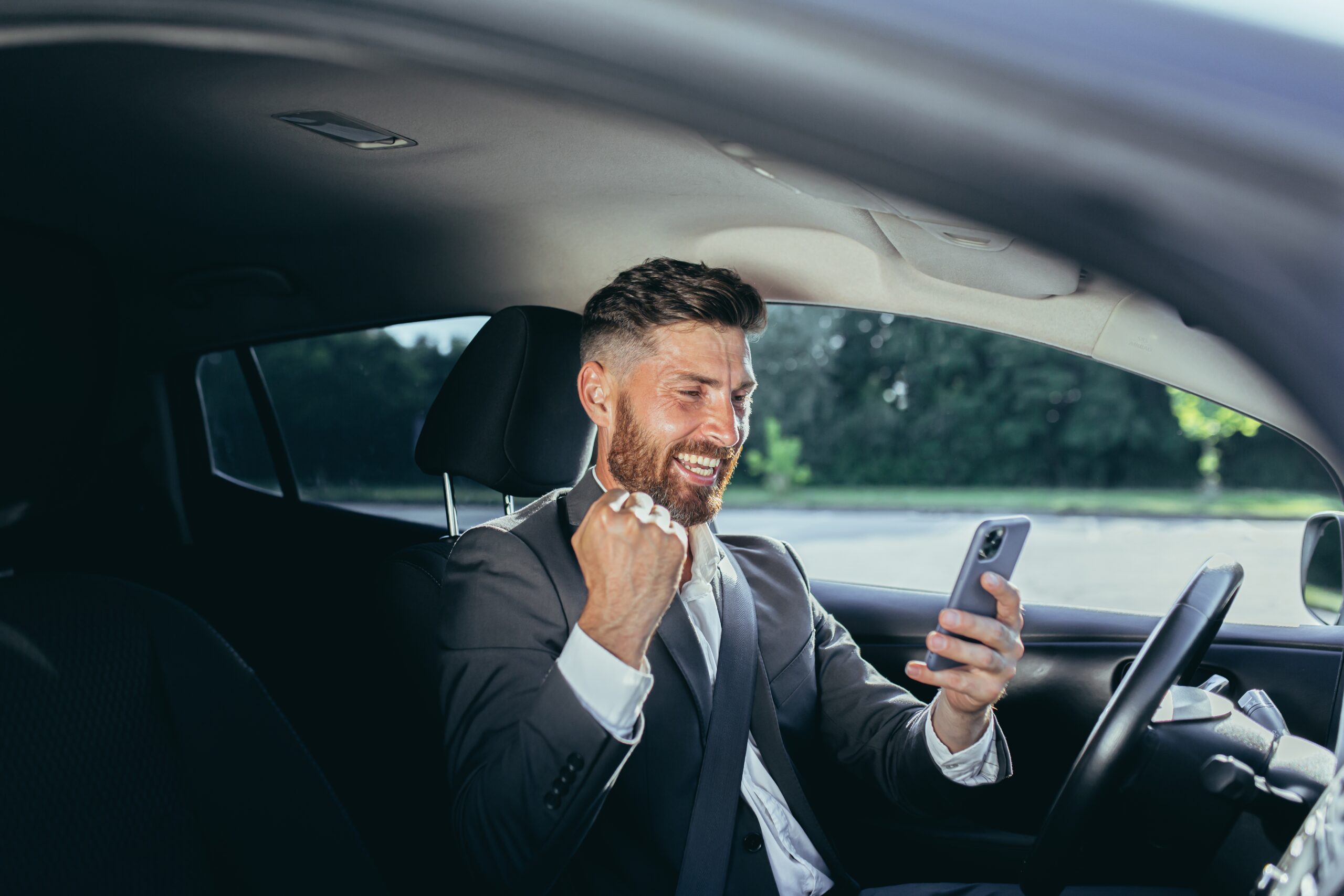 mężczyzna w garniturze z telefonem w ręce, siedzący w samochodzie