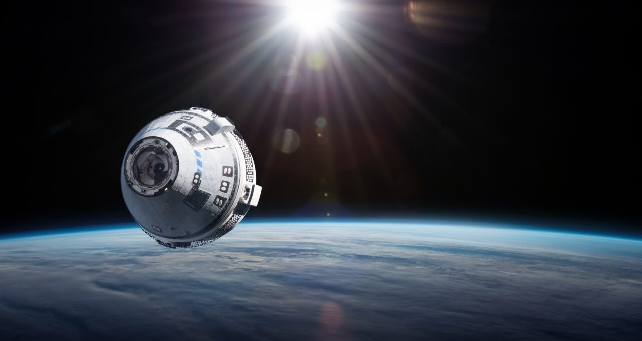 Statek kosmiczny Starliner na orbicie Ziemi z widoczną cienką warstwą atmosfery i promieniami słońca w tle.