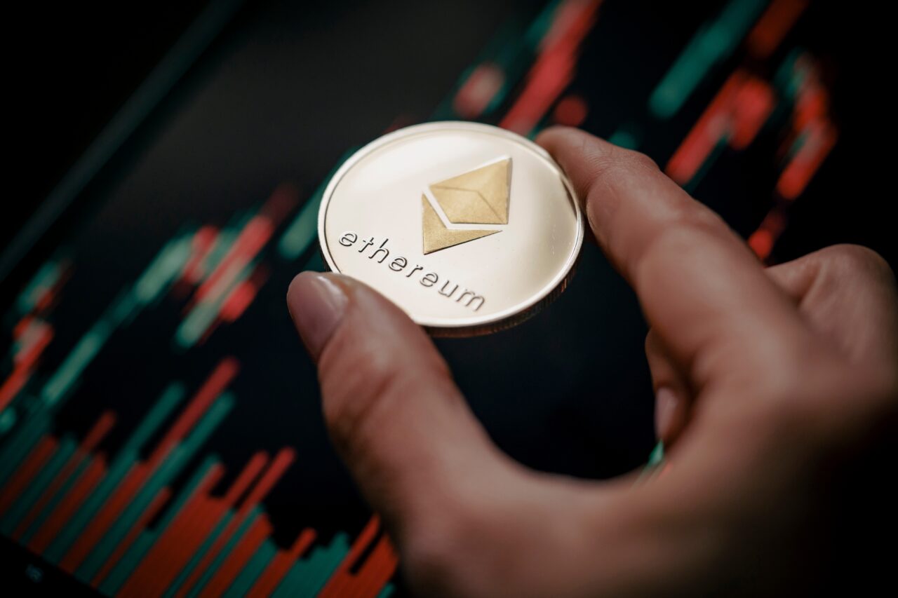 Ręka trzymająca monetę blockchain Ethereum na tle wykresu finansowego.