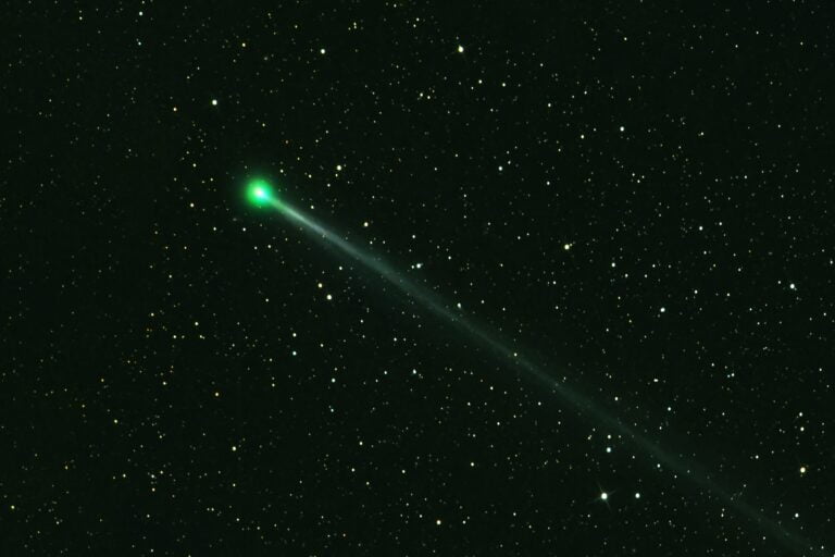 Zielona kometa na tle gwiaździstego nieba.