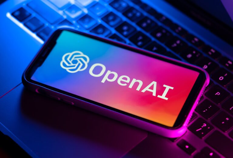 Smartfon z logo OpenAI na ekranie leżący na klawiaturze laptopa podświetlonym różowym i niebieskim światłem.
