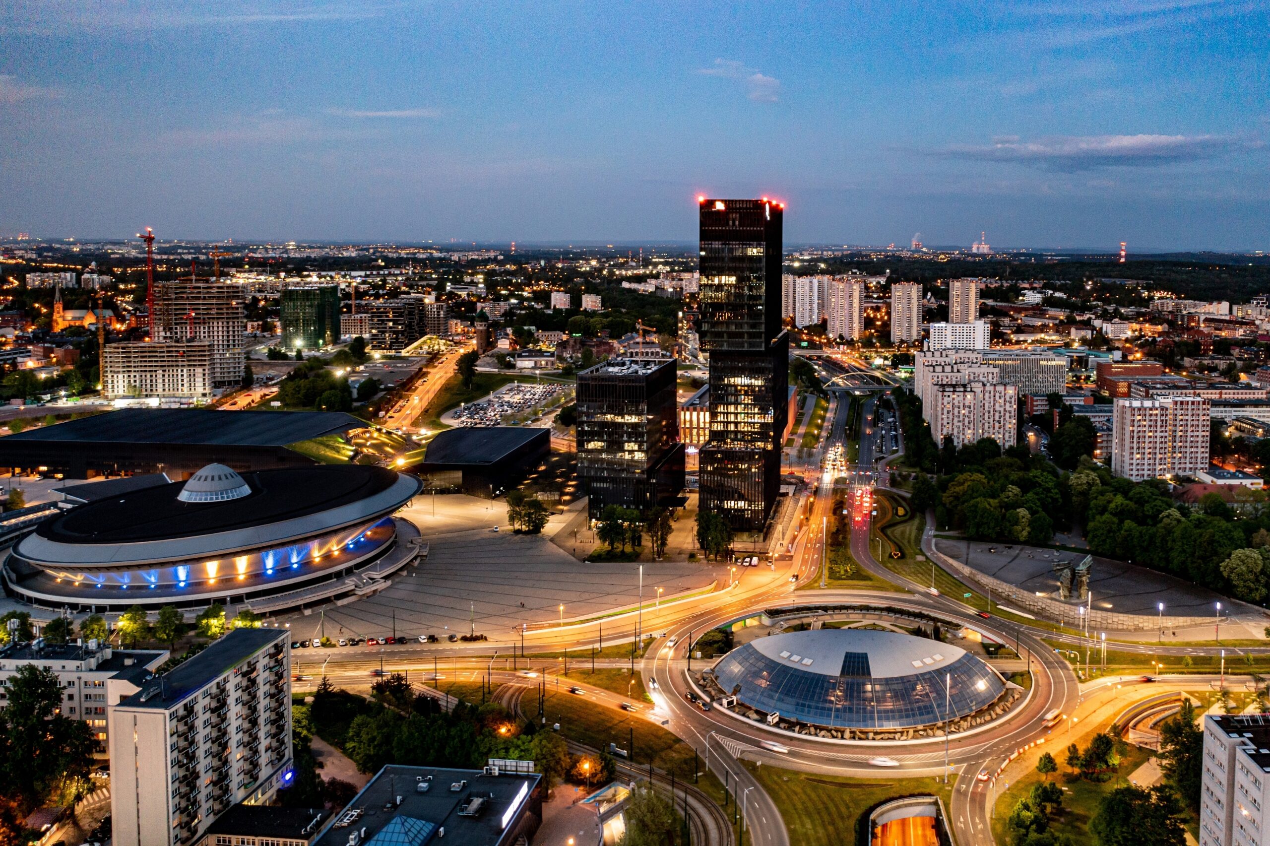 Widok na miasto Katowice z charakterystycznymi budynkami, w tym Spodek i biurowce KTW na pierwszym planie, w tle widoczna panorama miasta, zdjęcie wykonane o zmierzchu.