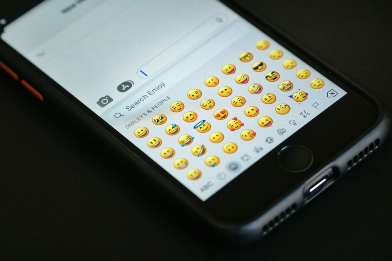 Smartfon z otwartą aplikacją do wiadomości, pokazującą listę emotikonów.