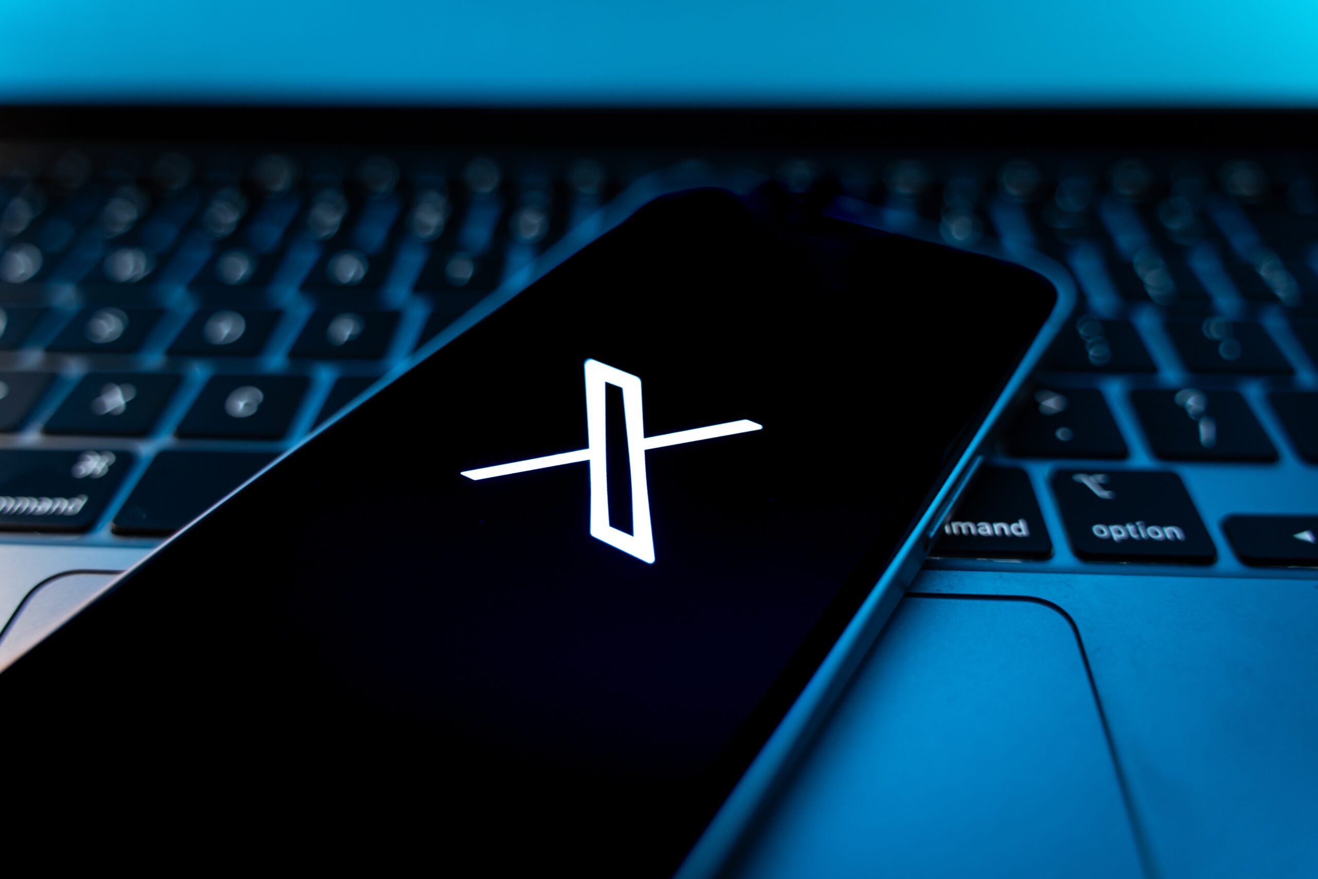 Telefon wyświetlający logo X położony na klawiaturze laptopa.