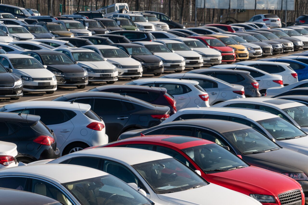 Zaparkowane samochody o różnych kolorach i modelach na dużym parkingu.