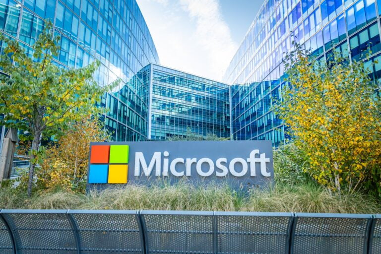 Siedziba firmy Microsoft z dużym logo na pierwszym planie, otoczona nowoczesnymi budynkami biurowymi i roślinnością.