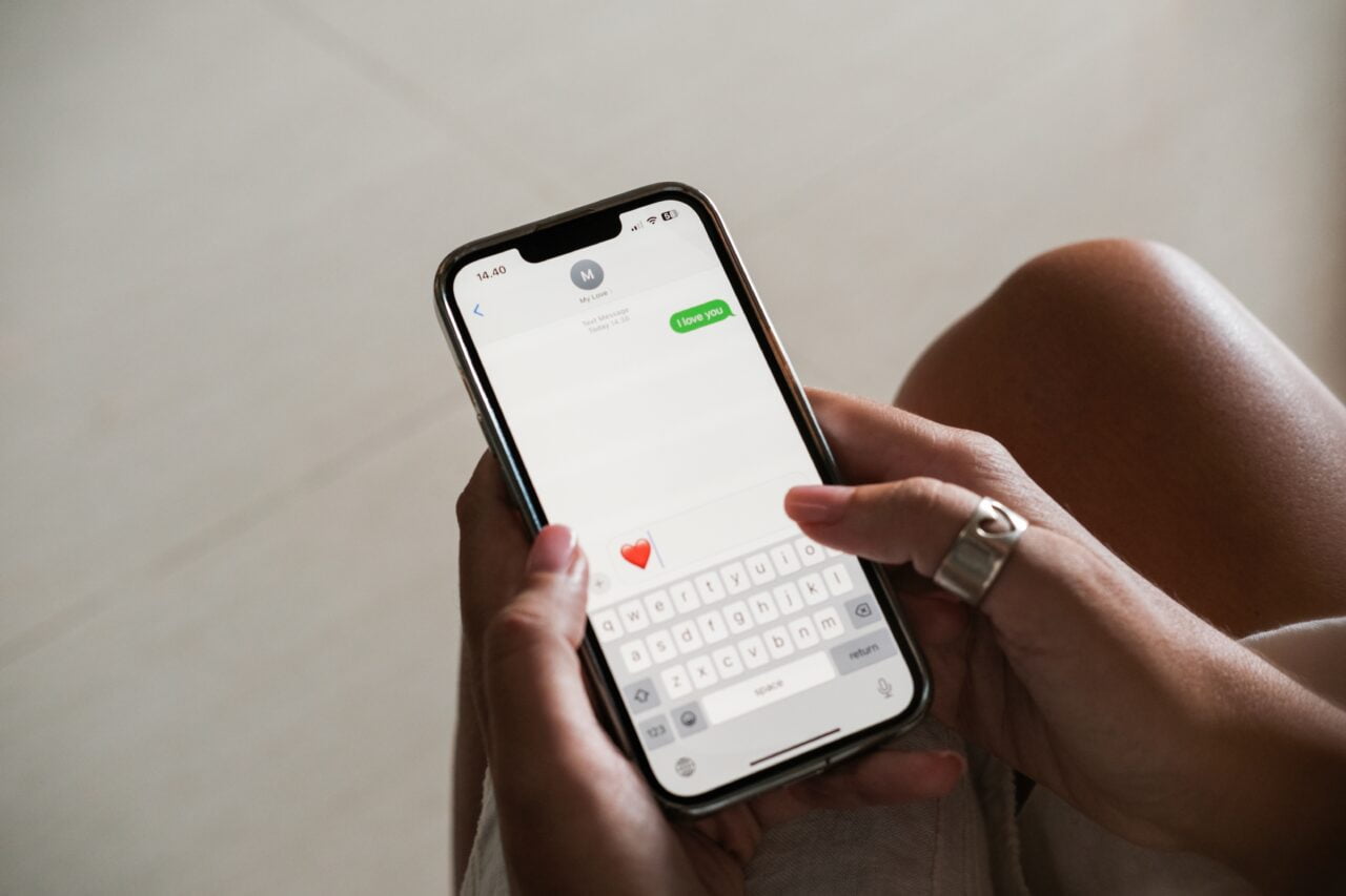 emoji w iOS 18 Osoba trzymająca iPhone z otwartą aplikacją wiadomości, pisząca wiadomość z ikoną serca.