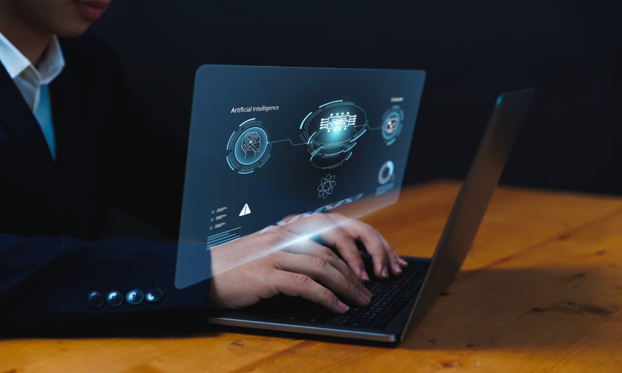Osoba w garniturze obsługująca laptop z futurystycznym interfejsem dotyczącym sztucznej inteligencji.