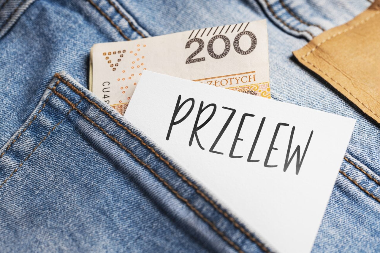 Banknot 200 złotych i kartka z napisem "PRZELEW" w kieszeni dżinsów.