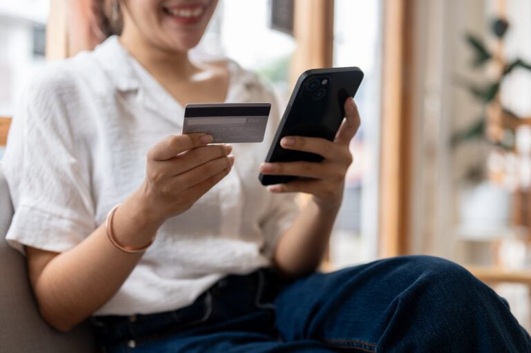 Kobieta trzymająca kartę kredytową i telefon komórkowy, uśmiechająca się.