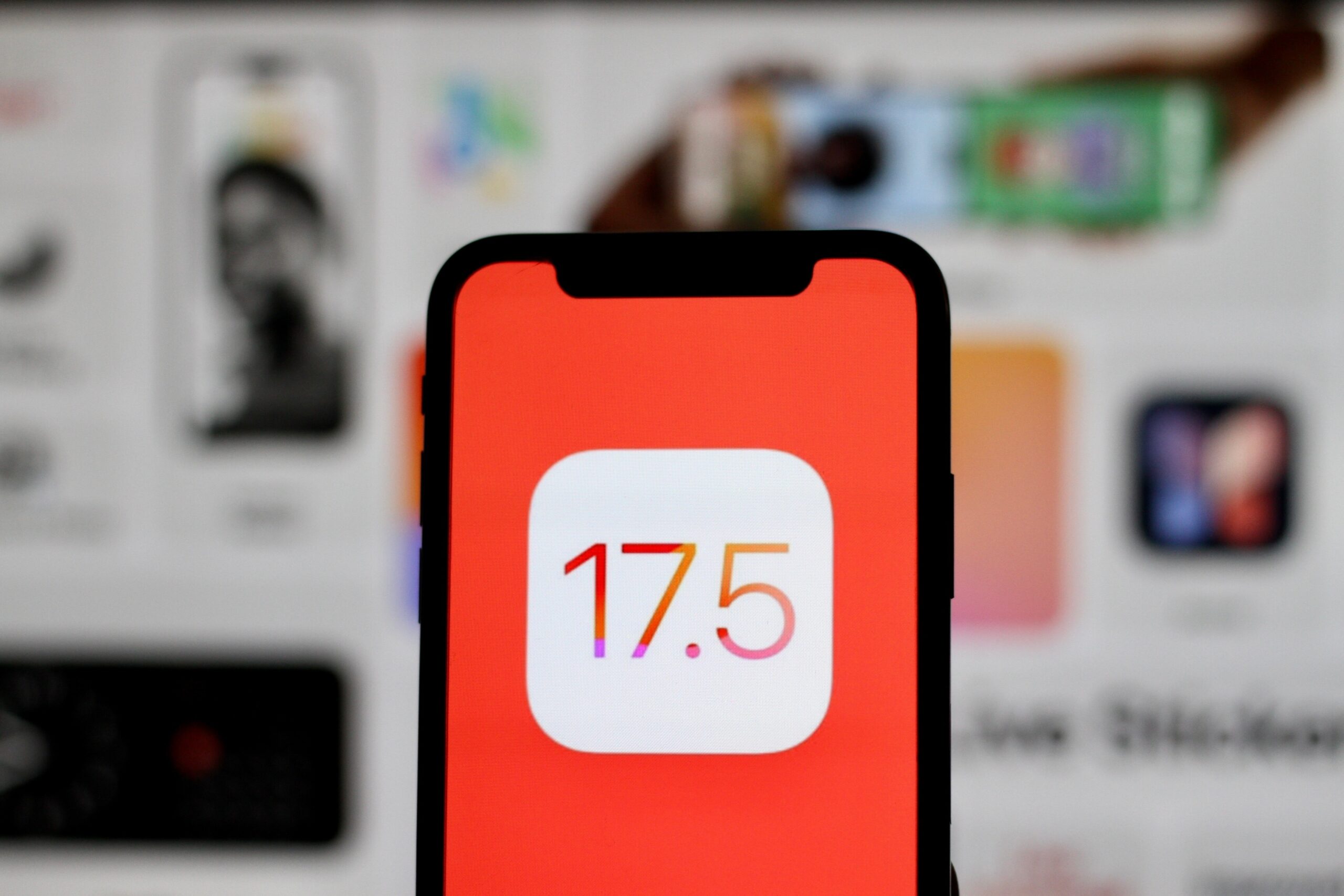 Ekran smartfona z logo iOS 17.5 na pomarańczowym tle.