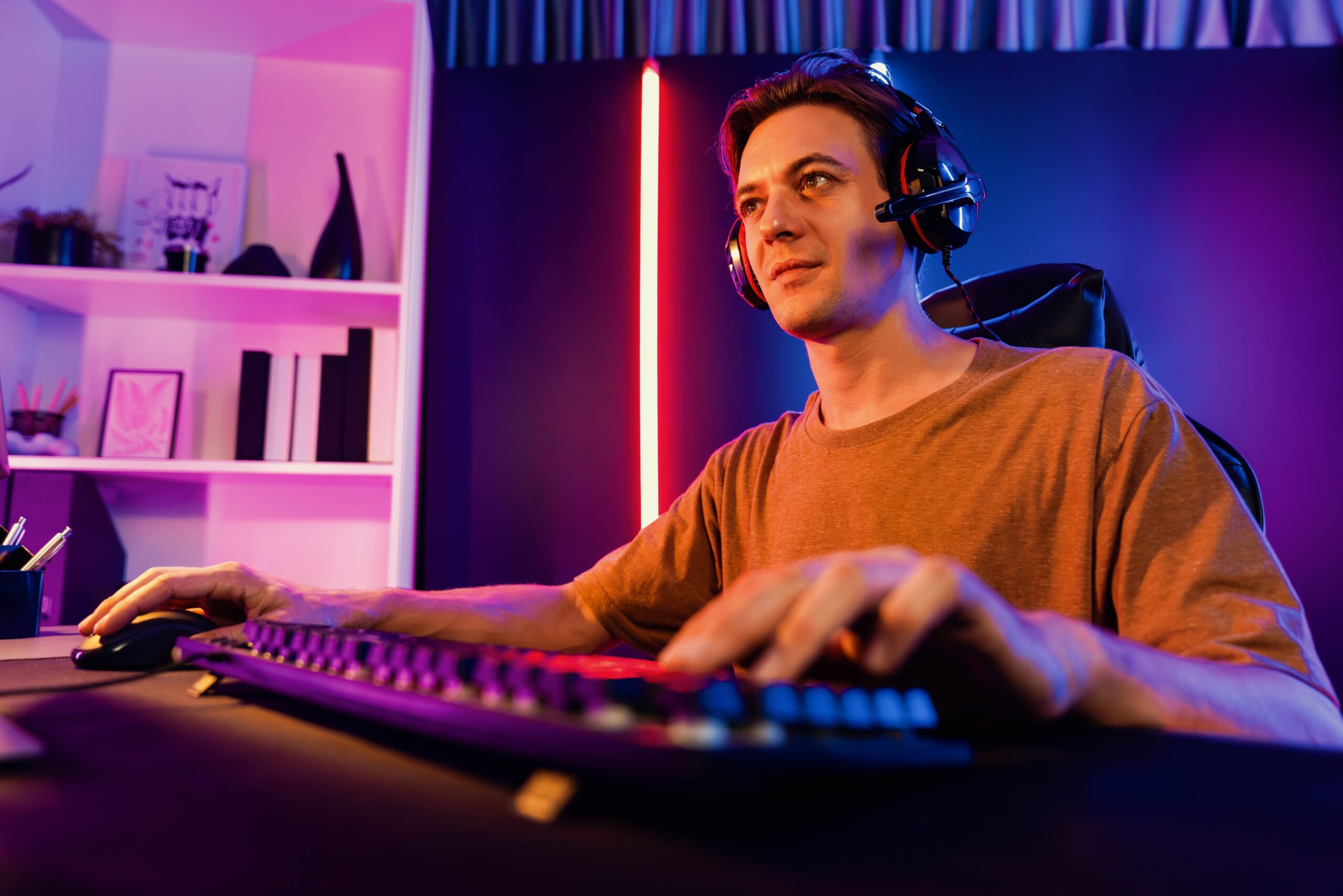 Mężczyzna z zestawem słuchawkowym siedzi przed komputerem w jasnym, kolorowym pokoju.