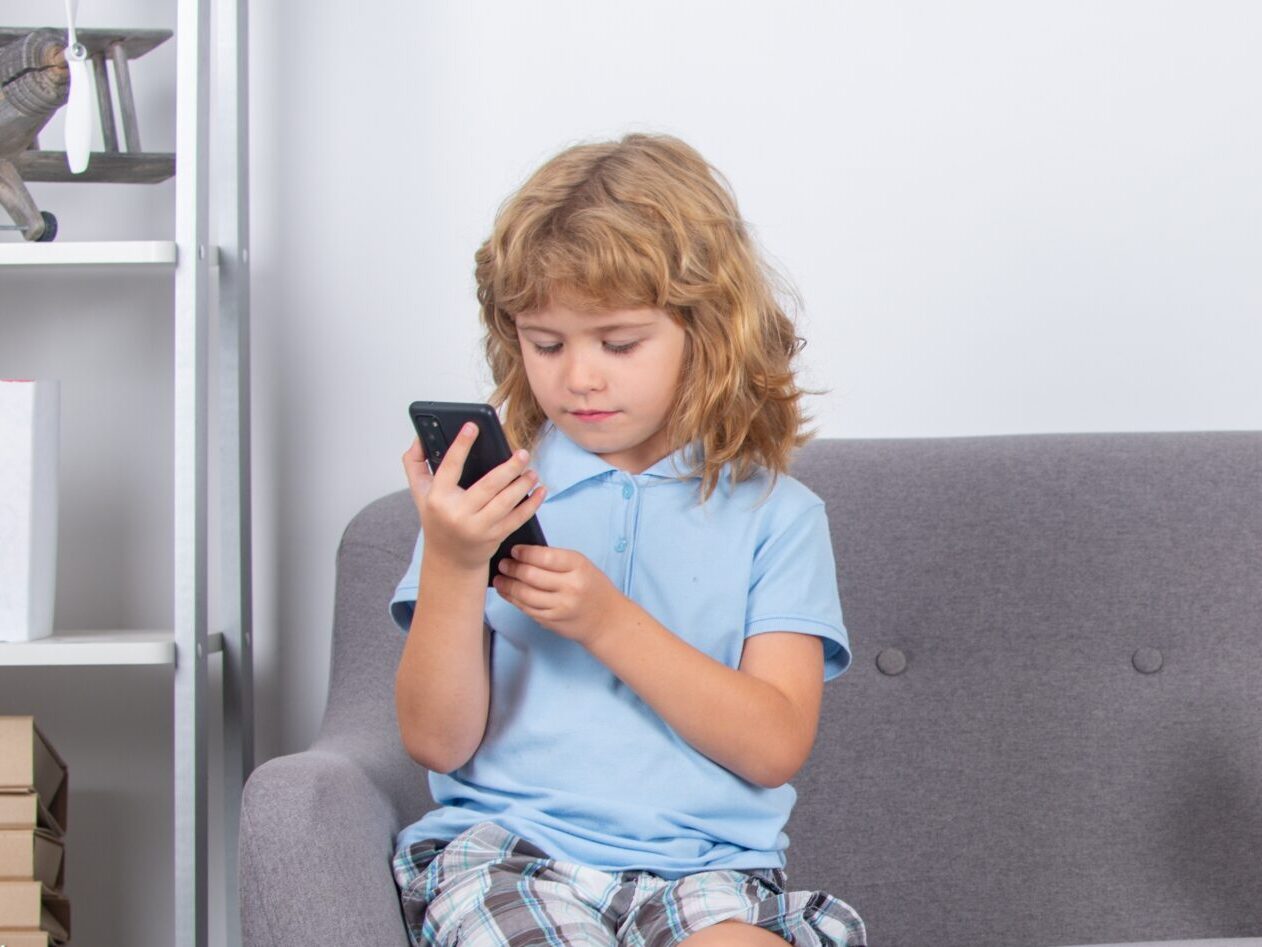 Dwoje dzieci siedzących na sofie, każde z nich trzyma smartfon.