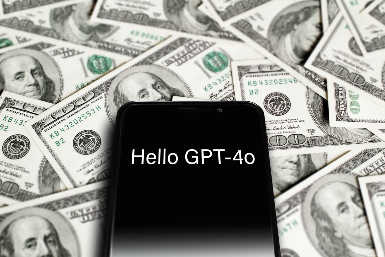 Telefon z napisem "Hello GPT-4" na tle banknotów stu dolarowych.