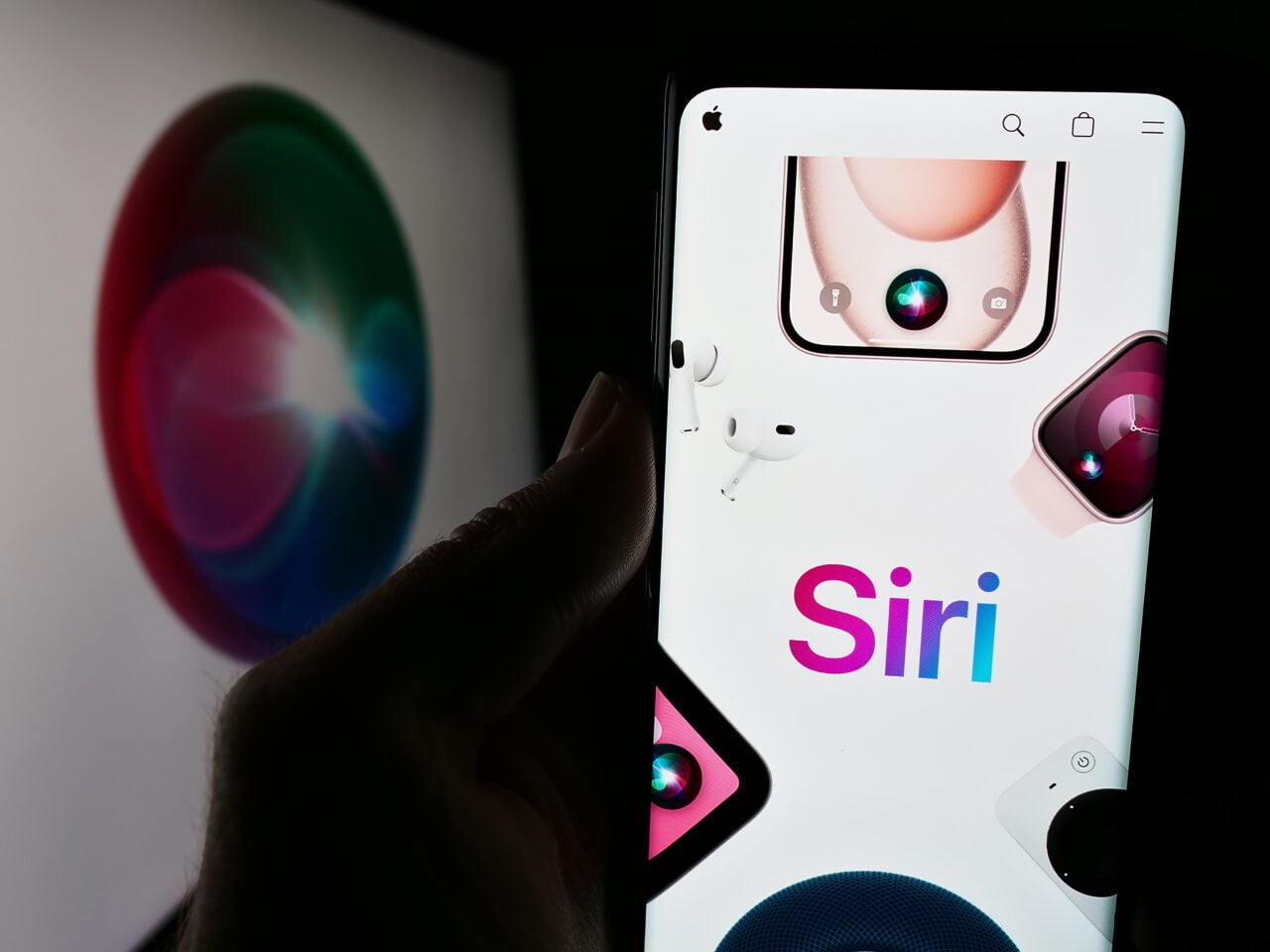 Ręka trzymająca smartfon z grafiką i logo Siri, w tle rozmyty ekran z logo Siri.