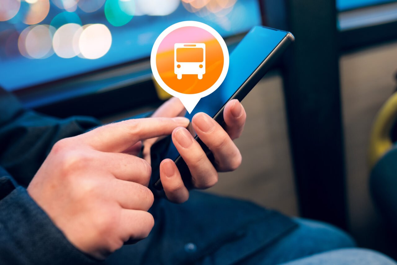 Osoba używa aplikacji komunikacji miejskiej na smartfonie w autobusie wieczorem.